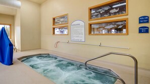 An indoor pool with a spa area, surrounded by framed artwork and a sign detailing spa regulations and pool capacity. - Quality Inn Kenai (Kenai)