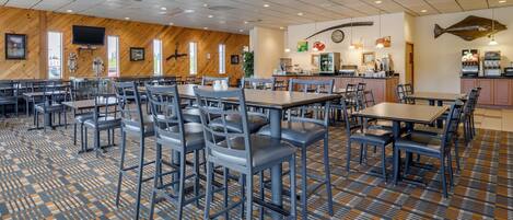 A spacious dining area with multiple tables and chairs, a kitchen area with a fish hanging on the wall, and a patterned carpet.