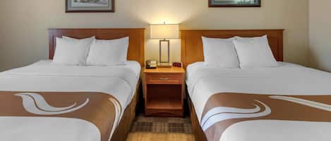 A hotel room with two beds, a nightstand with a lamp, and framed pictures on the wall.
