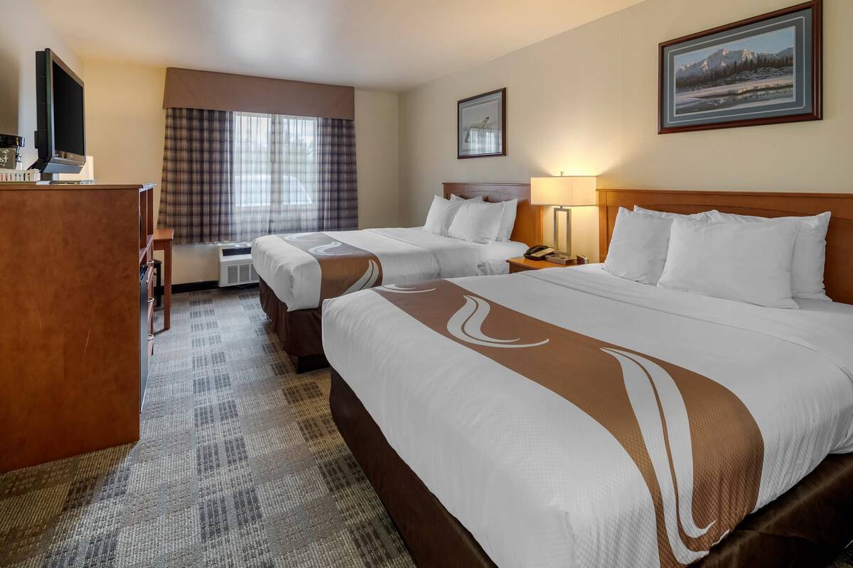 Habitación de hotel con dos camas, un escritorio, un televisor y una ventana con cortinas.