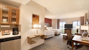 Habitación de hotel con cocina, cama con dos almohadas, televisor, escritorio con silla y ventana con vista a la ciudad.
