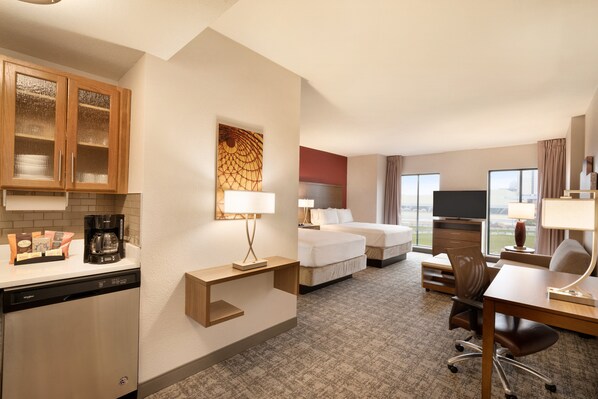 Habitación de hotel con cocina, cama con dos almohadas, televisor, escritorio con silla y ventana con vista a la ciudad.