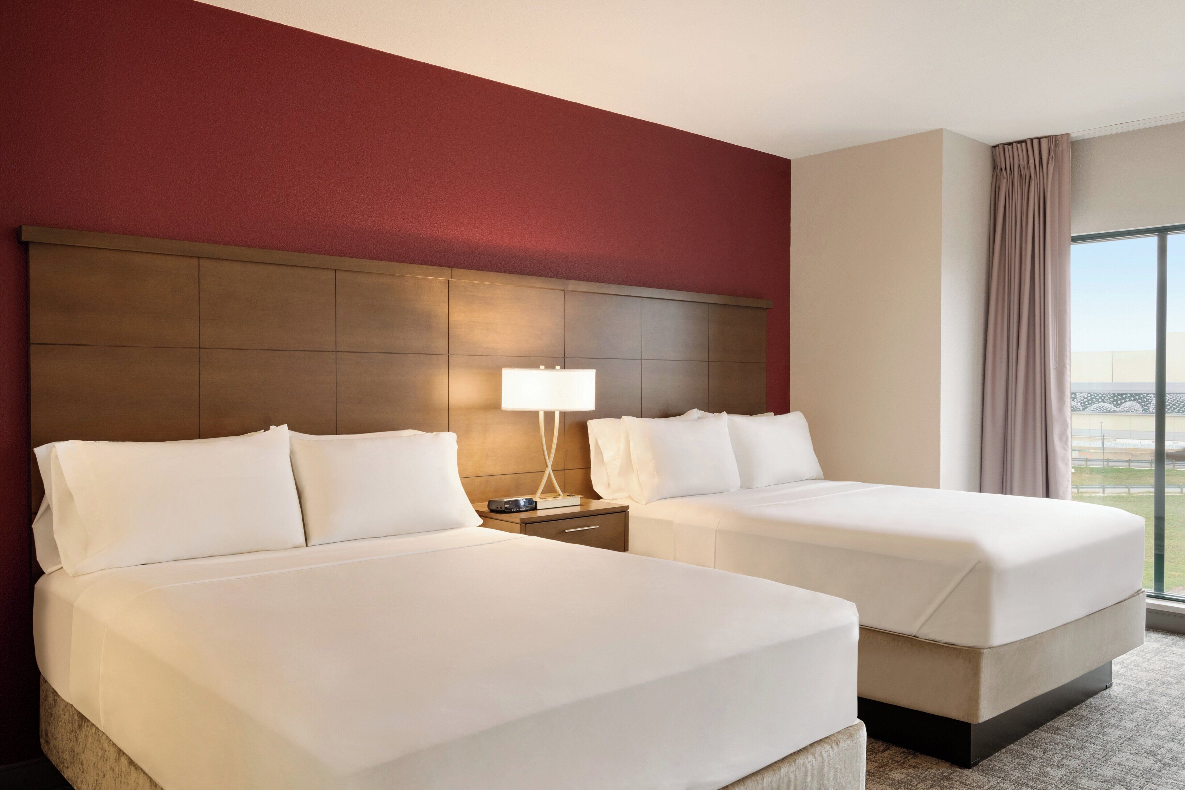 Habitació d'hotel amb dos llits, una meseta de nit amb una làmpada i una finestra gran amb vistes.