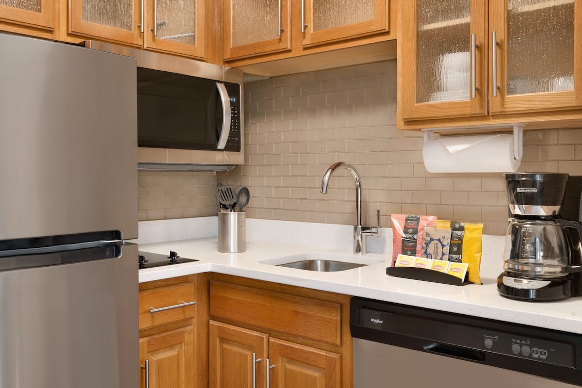 A modern kitchen with wooden cabinets, a stainless steel refrigerator, a microwave, a sink, and a coffee maker.