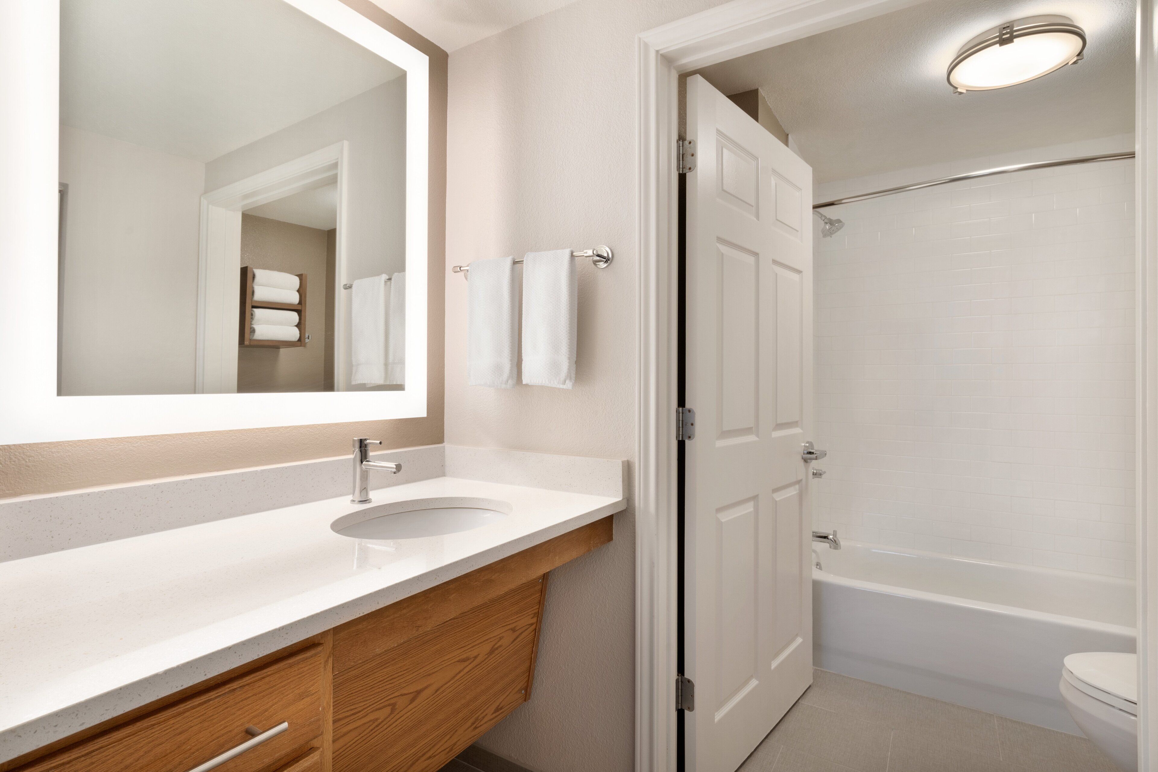 Un baño con lavamanos blanco, tocador de madera, un espejo grande y una bañera blanca.