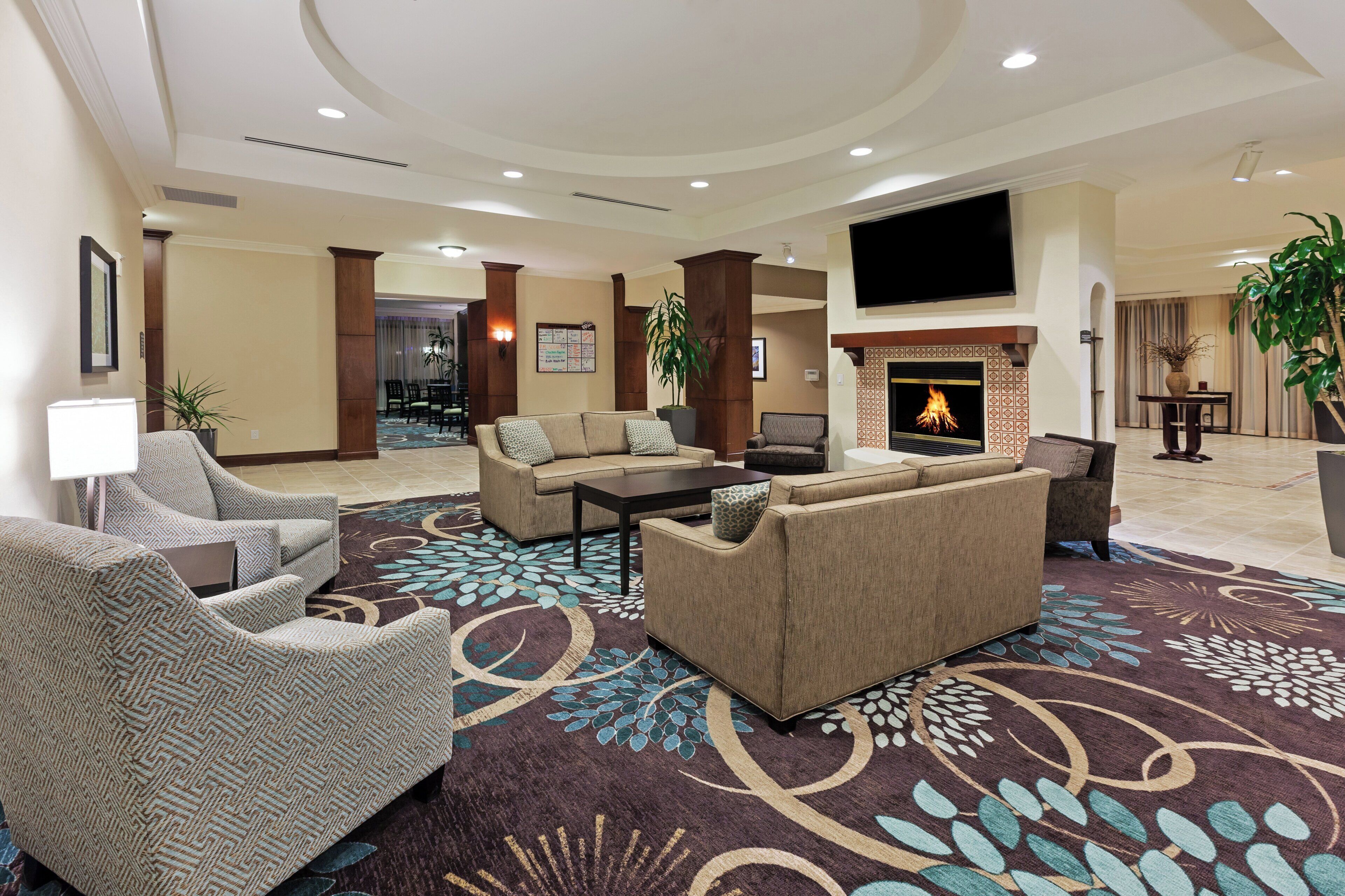 A hotel lobby with a fireplace, seating area, and a television mounted on the wall.