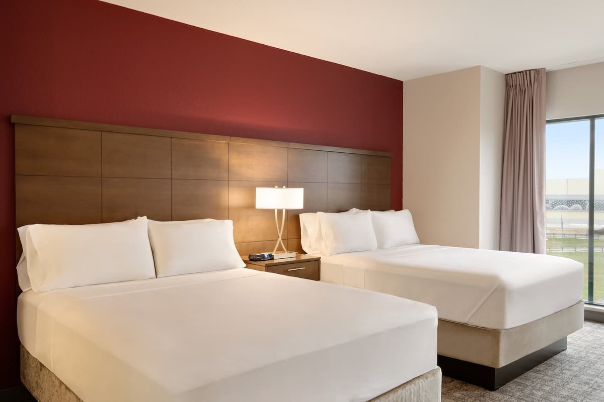 A hotel room with two beds, a nightstand with a lamp, and a large window with a view.