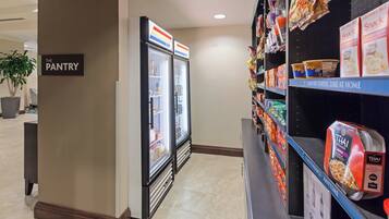 A hotel pantry area with refrigerated display cases and shelves stocked with snacks and beverages.