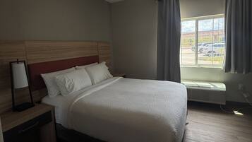Ein Hotelzimmer mit Bett, Nachttisch, Lampe, einem Fenster mit Vorhängen und einer Klimaanlage.