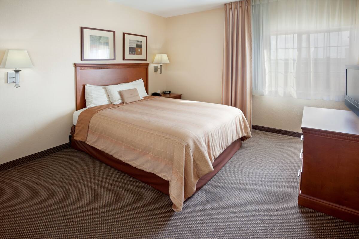 A hotel room with a large bed, two bedside tables, a TV, and a window with curtains.