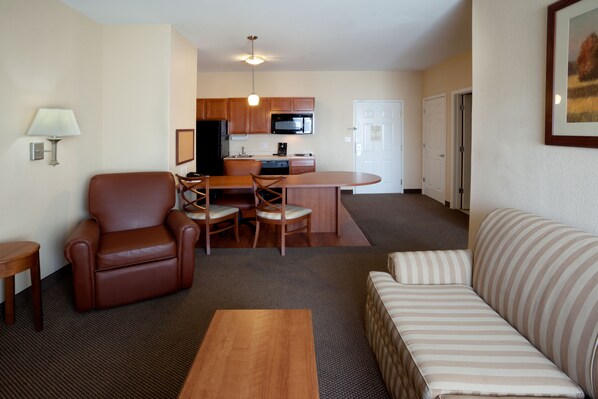 A compact living space with a kitchenette, a brown leather armchair, a striped sofa, and a wooden coffee table. - Candlewood Suites Corpus Christi-Spid by IHG (Corpus Christi)