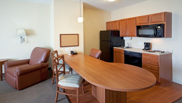 A compact kitchen with a refrigerator, microwave, and dishwasher. There is a dining area with a table and chairs. - Candlewood Suites Corpus Christi-Spid by IHG (Corpus Christi)
