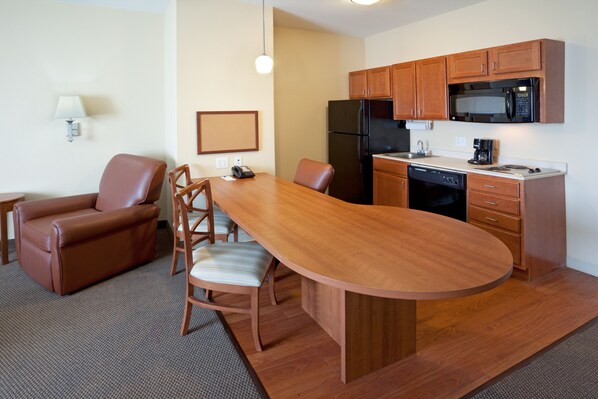 A compact kitchen with a refrigerator, microwave, and dishwasher. There is a dining area with a table and chairs. - Candlewood Suites Corpus Christi-Spid by IHG (Corpus Christi)