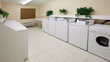 A laundry room with four washing machines, a dryer, a vent, and a window with blinds.