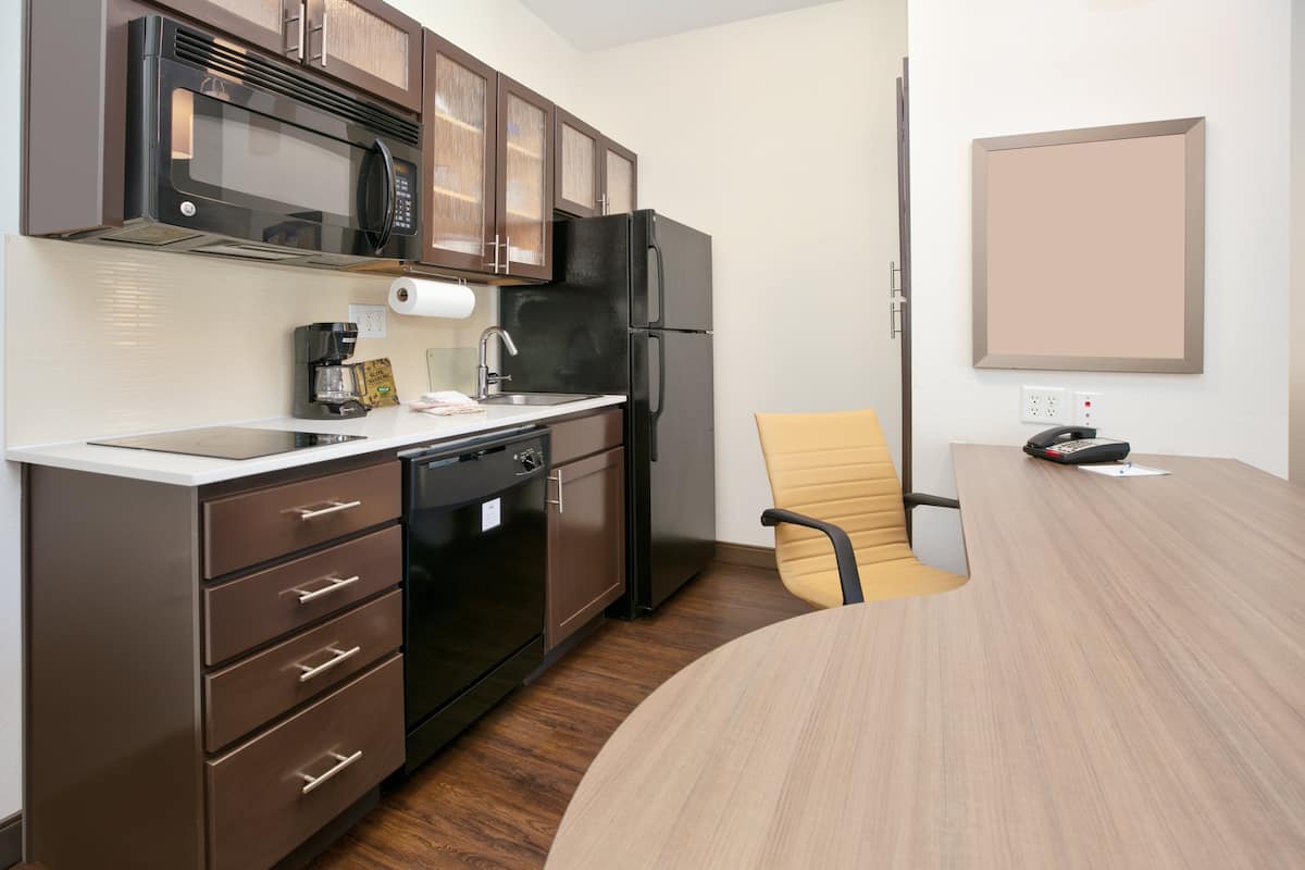 A modern kitchen with a microwave, refrigerator, and dishwasher. There is a wooden dining table and a single chair.
