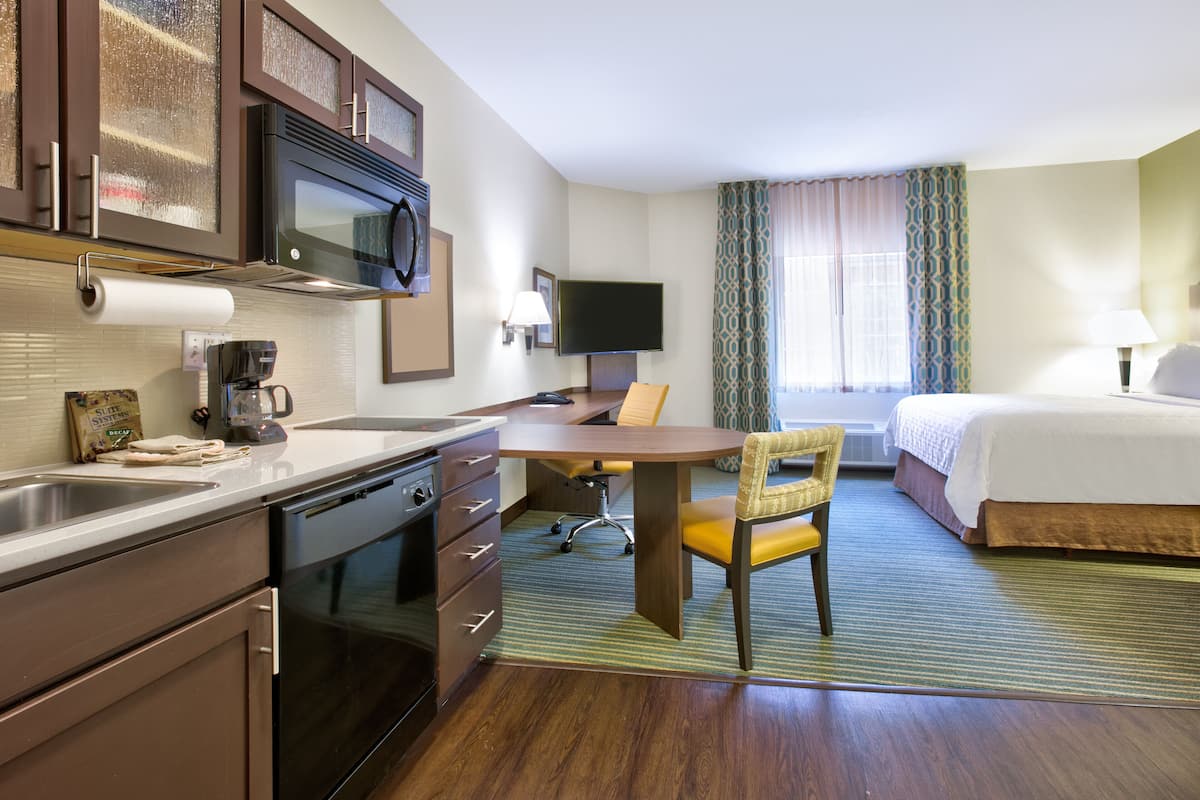 A hotel room with a kitchenette, a bed, a desk, and a TV.