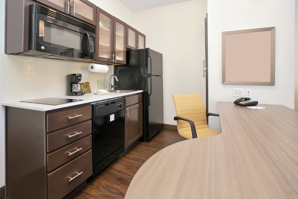 Una cocina moderna con microondas, refrigerador y lavavajillas. Hay una mesa de madera y una sola silla.