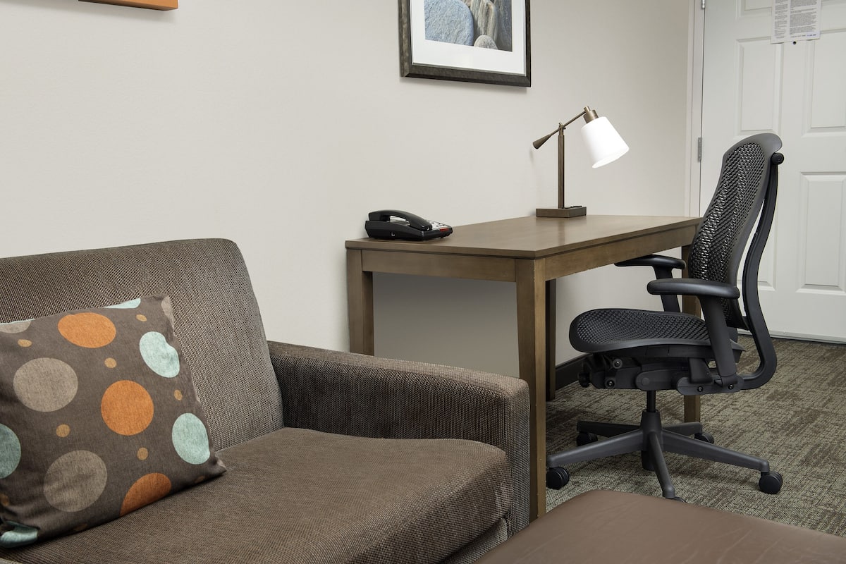 A room with a brown sofa, a black office chair, a wooden desk, and a lamp.