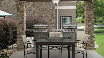 Un patio al aire libre con pared de piedra, una parrilla y una mesa con sillas.