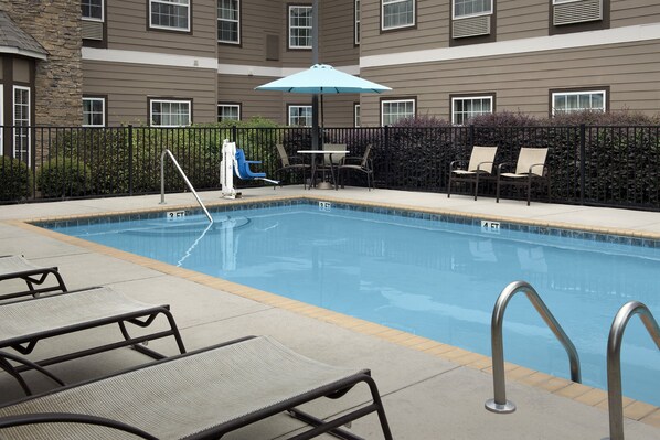 A swimming pool with lounge chairs, a table, and an umbrella. - Staybridge Suites Greenville I-85 Woodruff Road by IHG (Greenville)