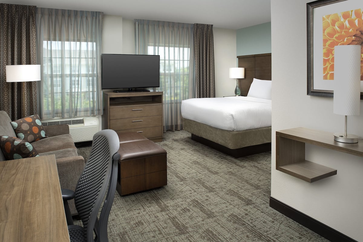 A hotel room with a bed, a TV, a desk, and a chair.