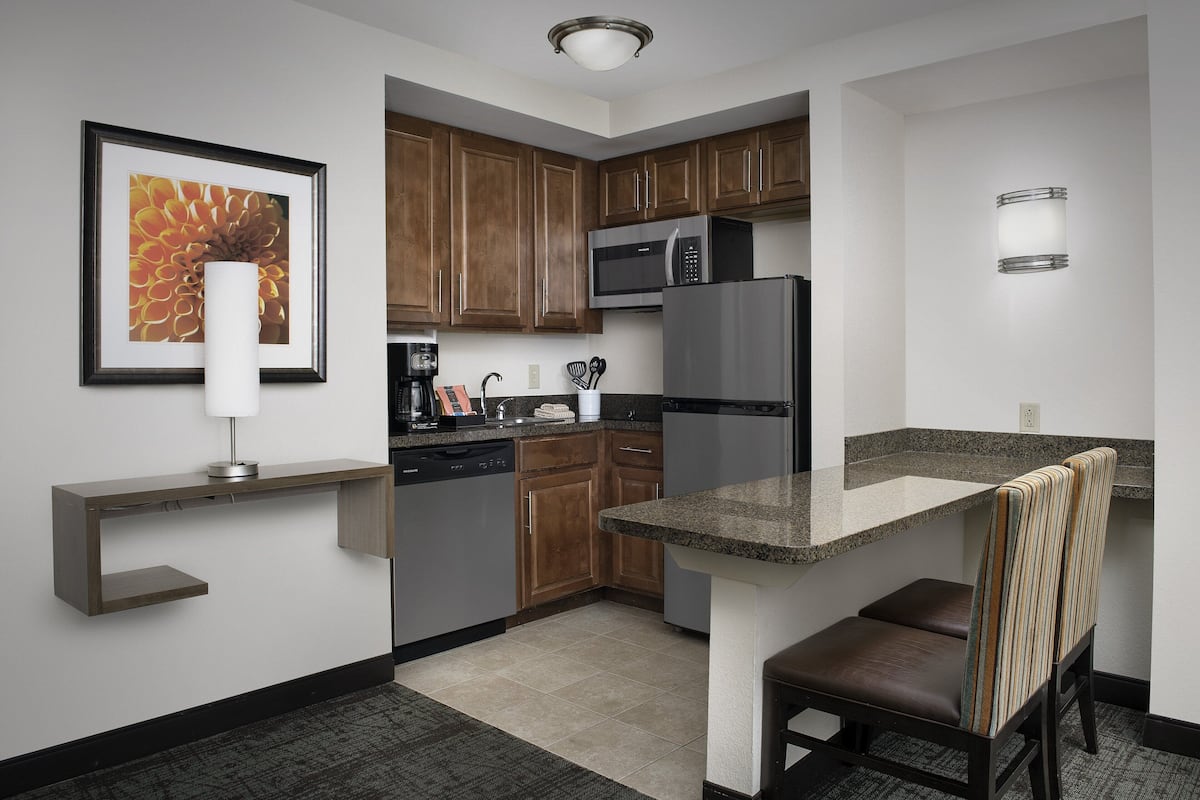 A modern kitchen with wooden cabinets, a stainless steel refrigerator, a microwave, and a built-in island with seating.