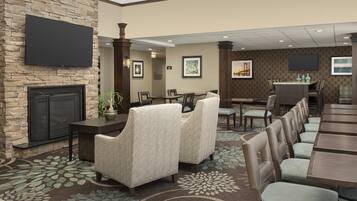 A hotel lobby with a stone fireplace, seating area with patterned chairs, a dining area with tables, and artwork on the walls.