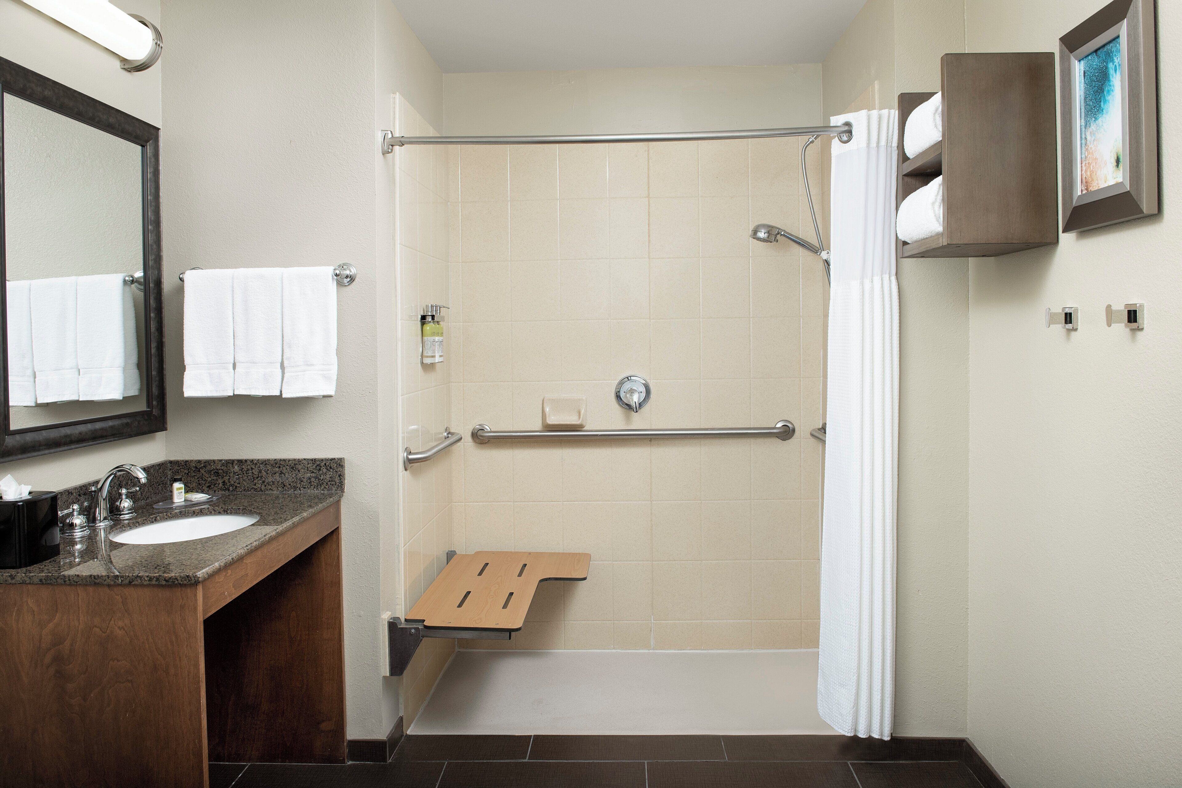A hotel bathroom with a shower, a sink, and a mirror.