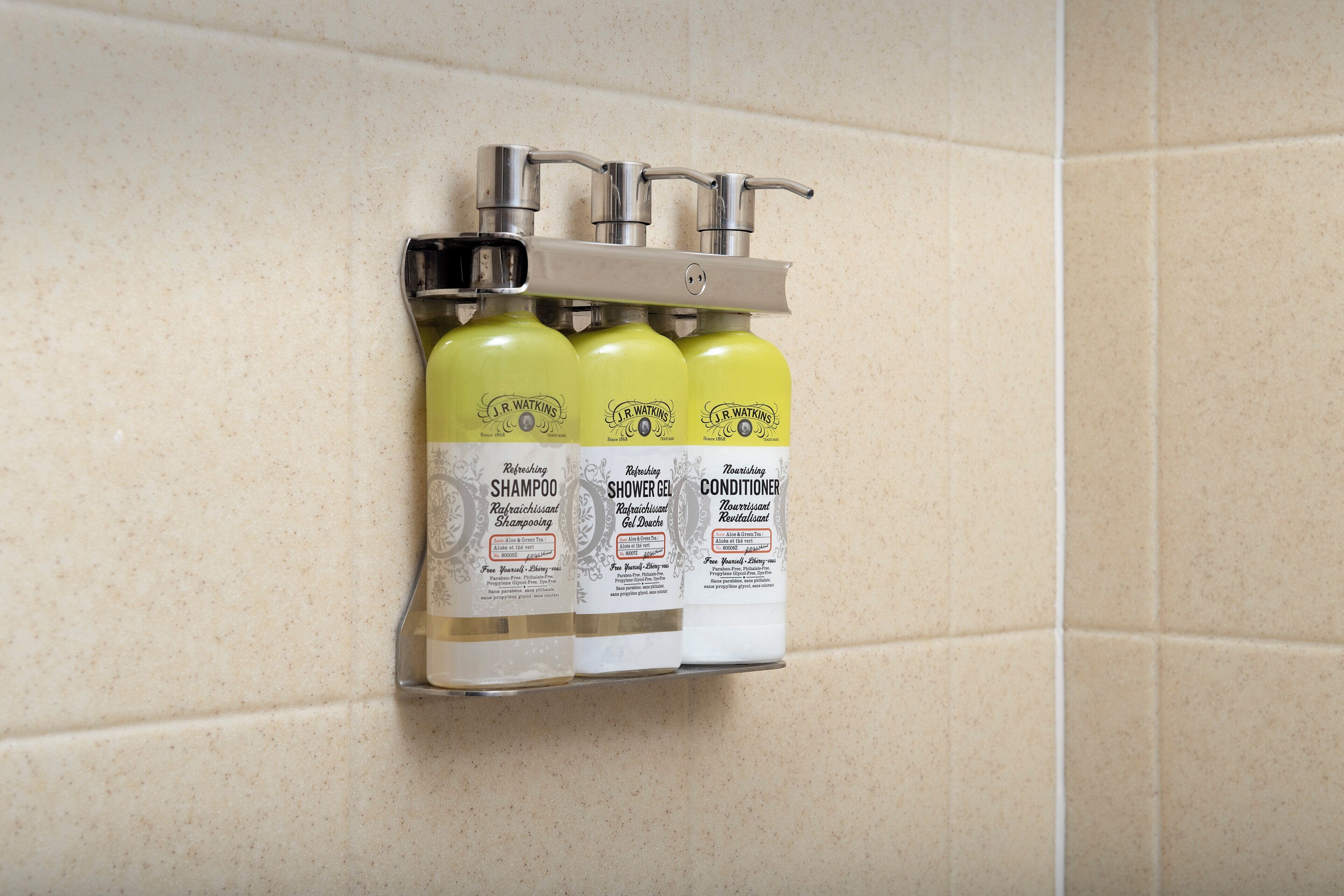 A bathroom with a wall-mounted shelf holding three bottles of J.R. Watkins products: shampoo, shower gel, and conditioner.