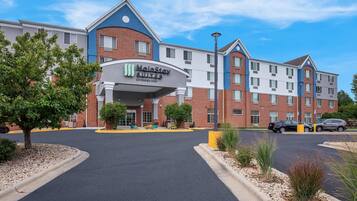 Un hotel MainStay Suites Extended Stay con fachada de ladrillo, varias ventanas y un estacionamiento con coches.