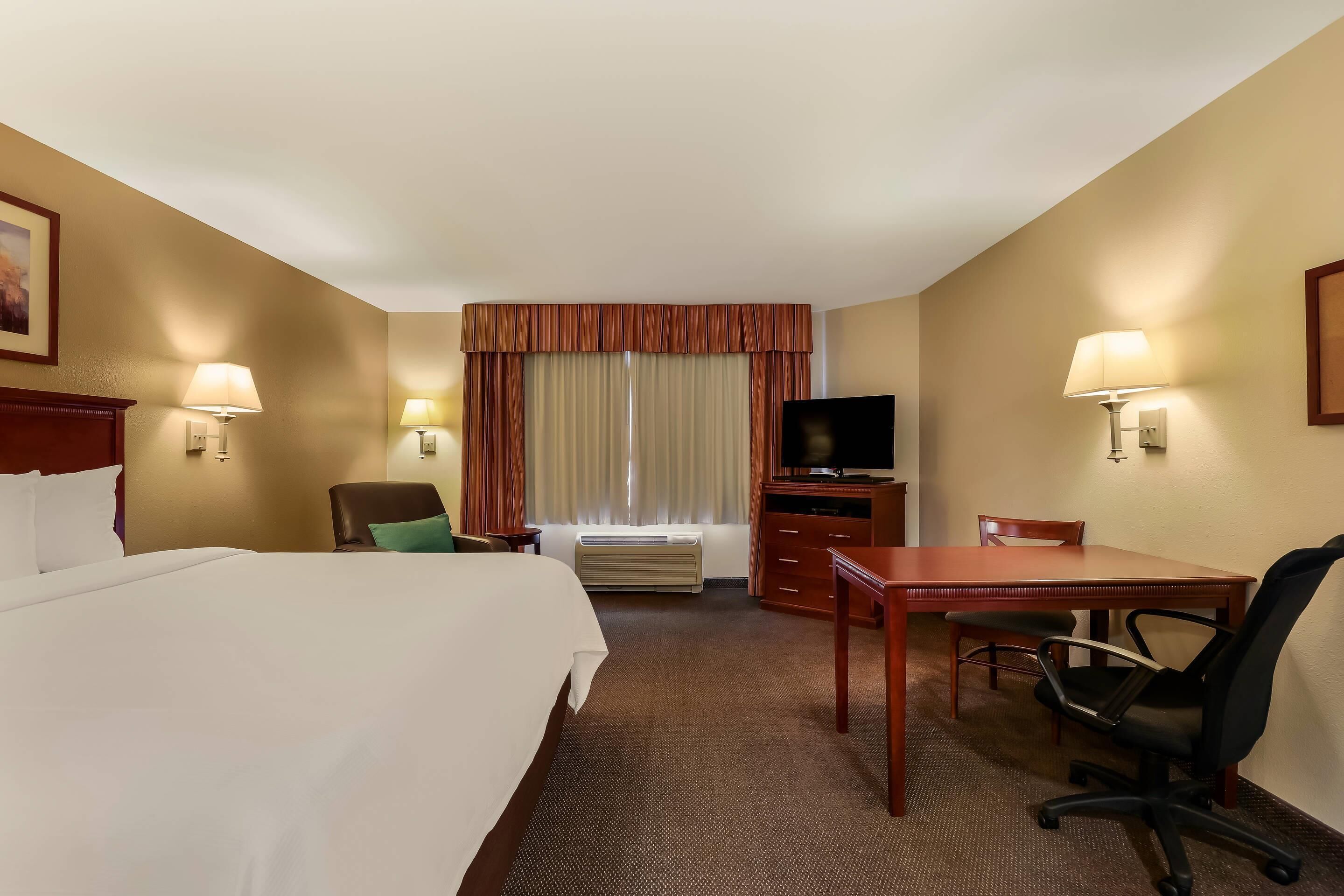 A hotel room with a large bed, a desk, a chair, a television, and a window with curtains.