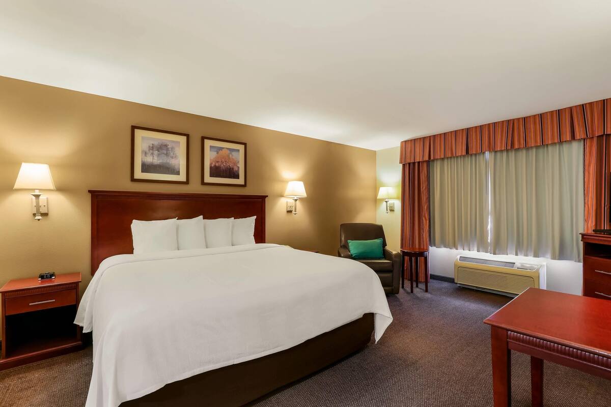 Une chambre d’hôtel avec un grand lit, deux lampes de chevet, une chaise, une table, un radiateur et deux tableaux encadrés au mur.