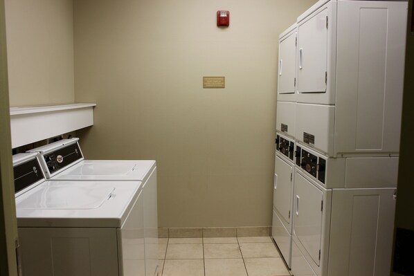 A laundry room with stacked washers and dryers, a fire alarm, and a plaque on the wall.