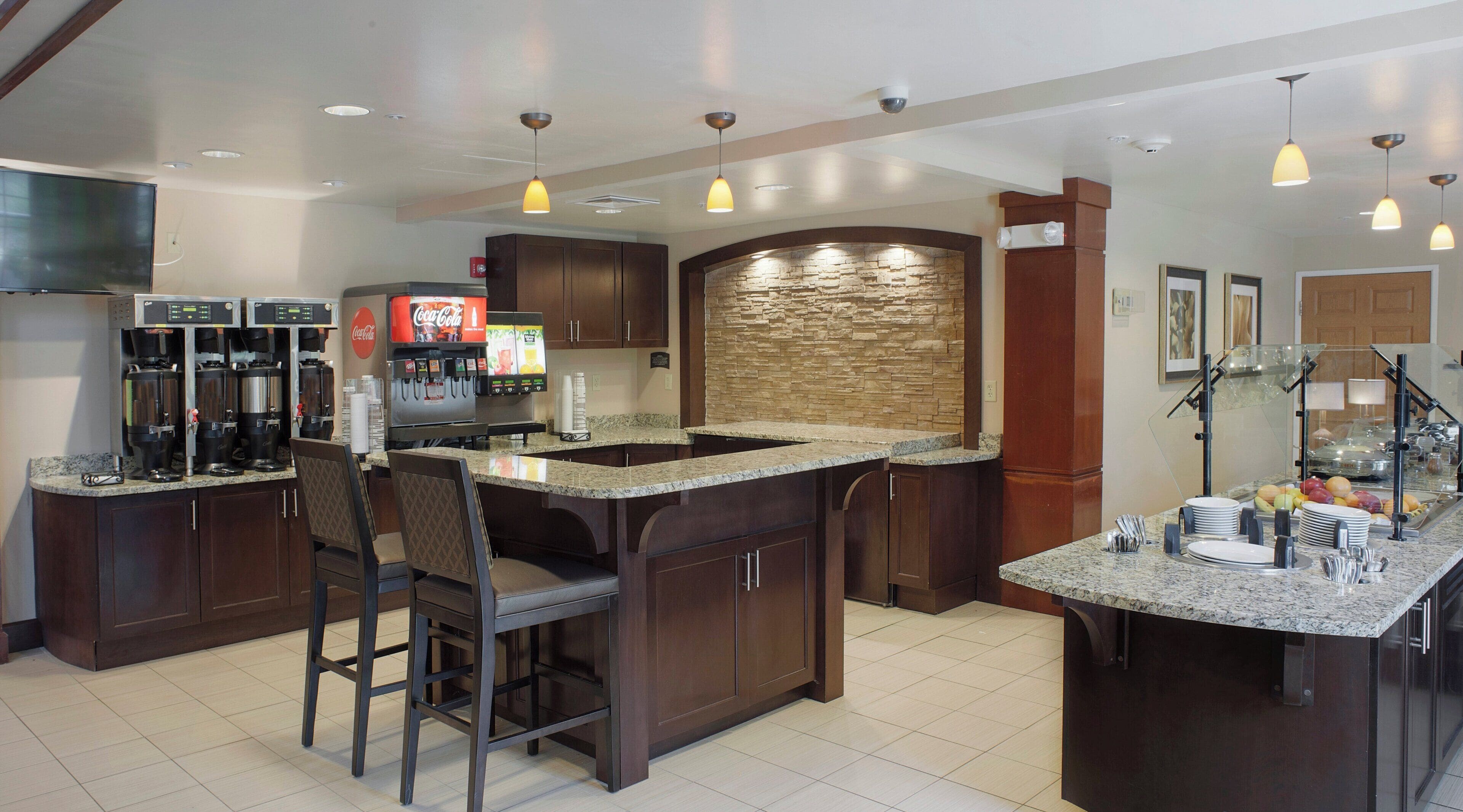 A modern kitchen with a central island, bar stools, a coffee station, and a stone accent wall.