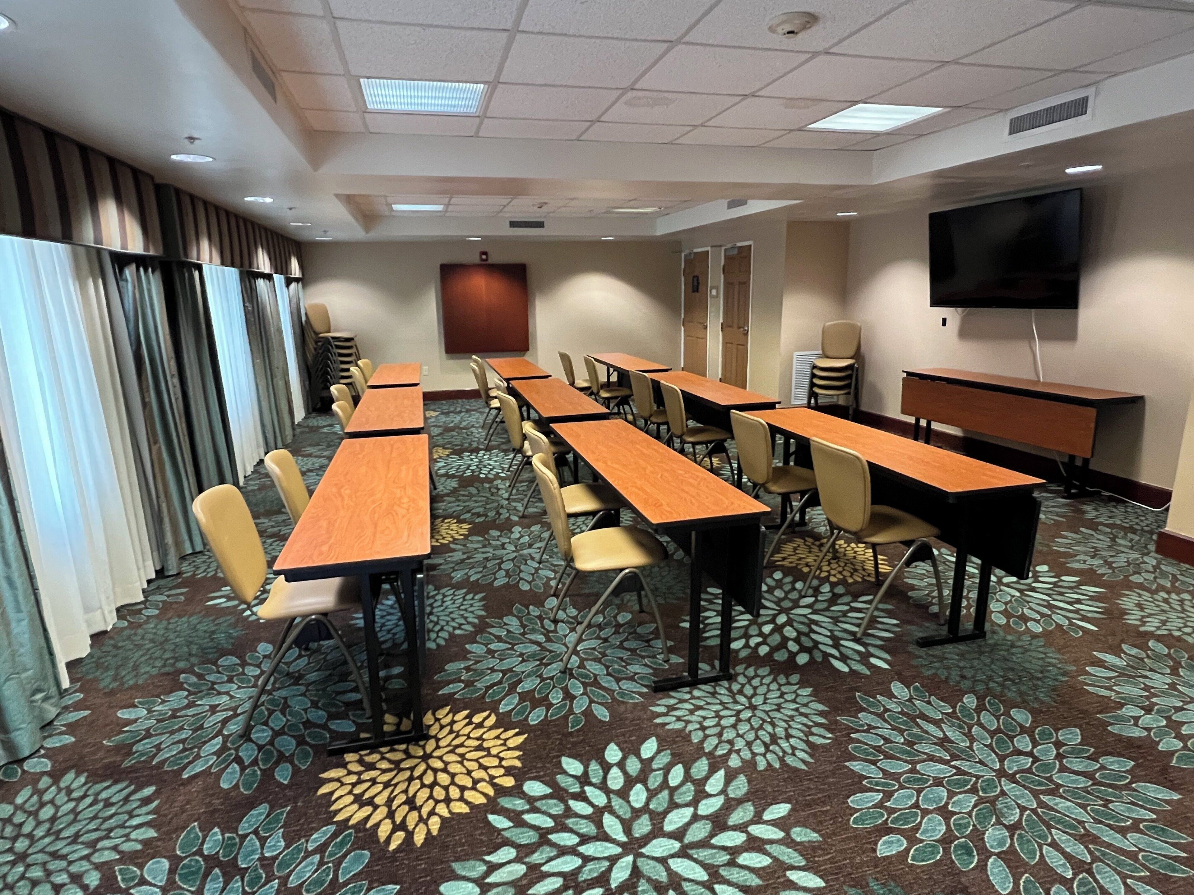 A conference room with multiple tables and chairs, a flat-screen TV, and a patterned carpet.