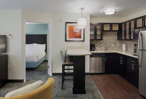 Una habitación de hotel compacta con cama, una pequeña zona de estar, kitchenette y baño.