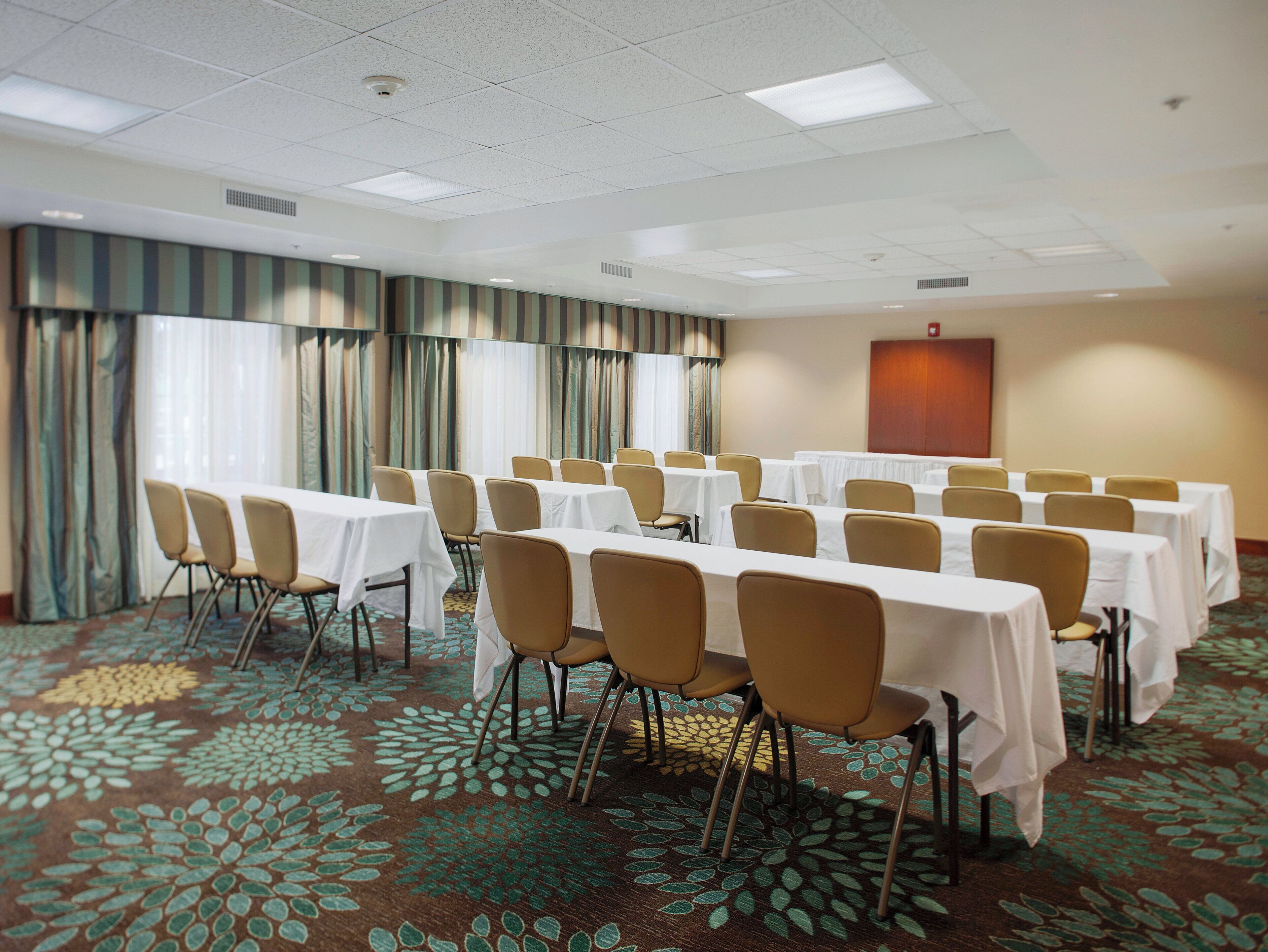 A conference room with multiple tables and chairs, a patterned carpet, and a plain wall with a door.