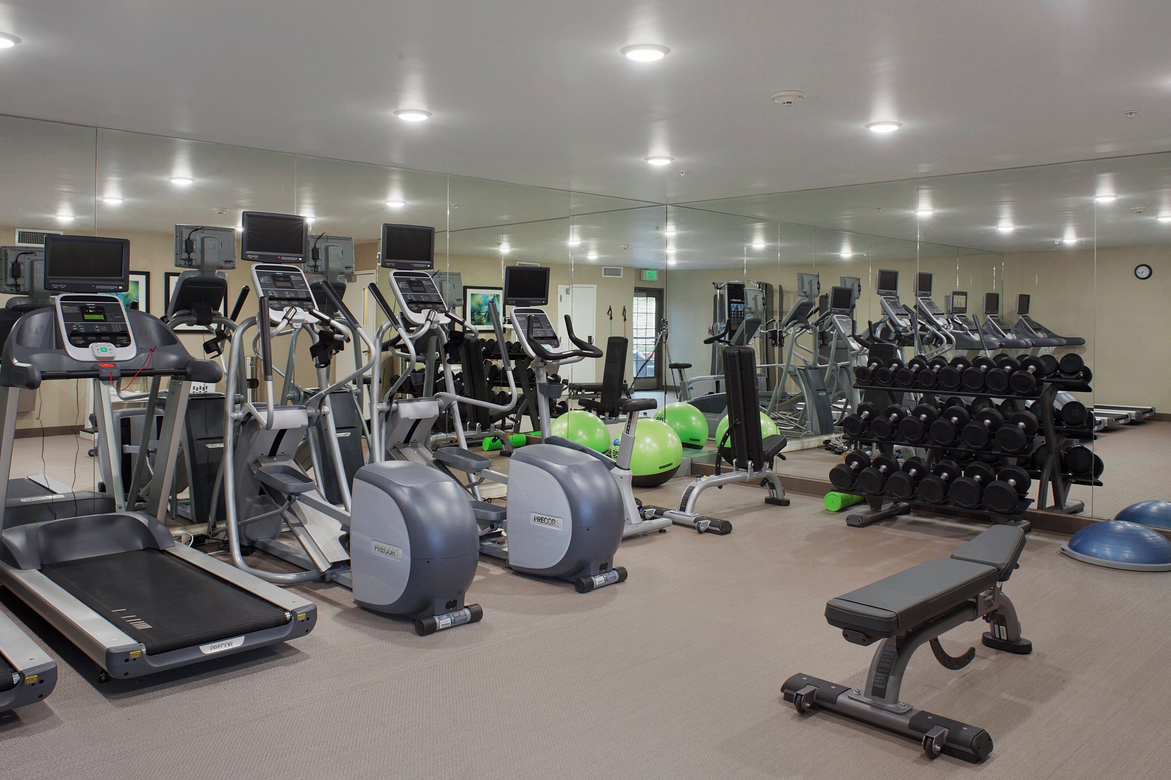 Un gimnasio con diversos equipos de ejercicio, incluyendo cintas de correr, elípticas y estaciones de levantamiento de pesas.