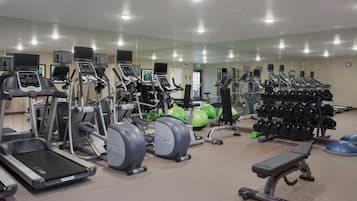 Un gimnasio con diversos equipos de ejercicio, incluyendo cintas de correr, elípticas y estaciones de levantamiento de pesas.
