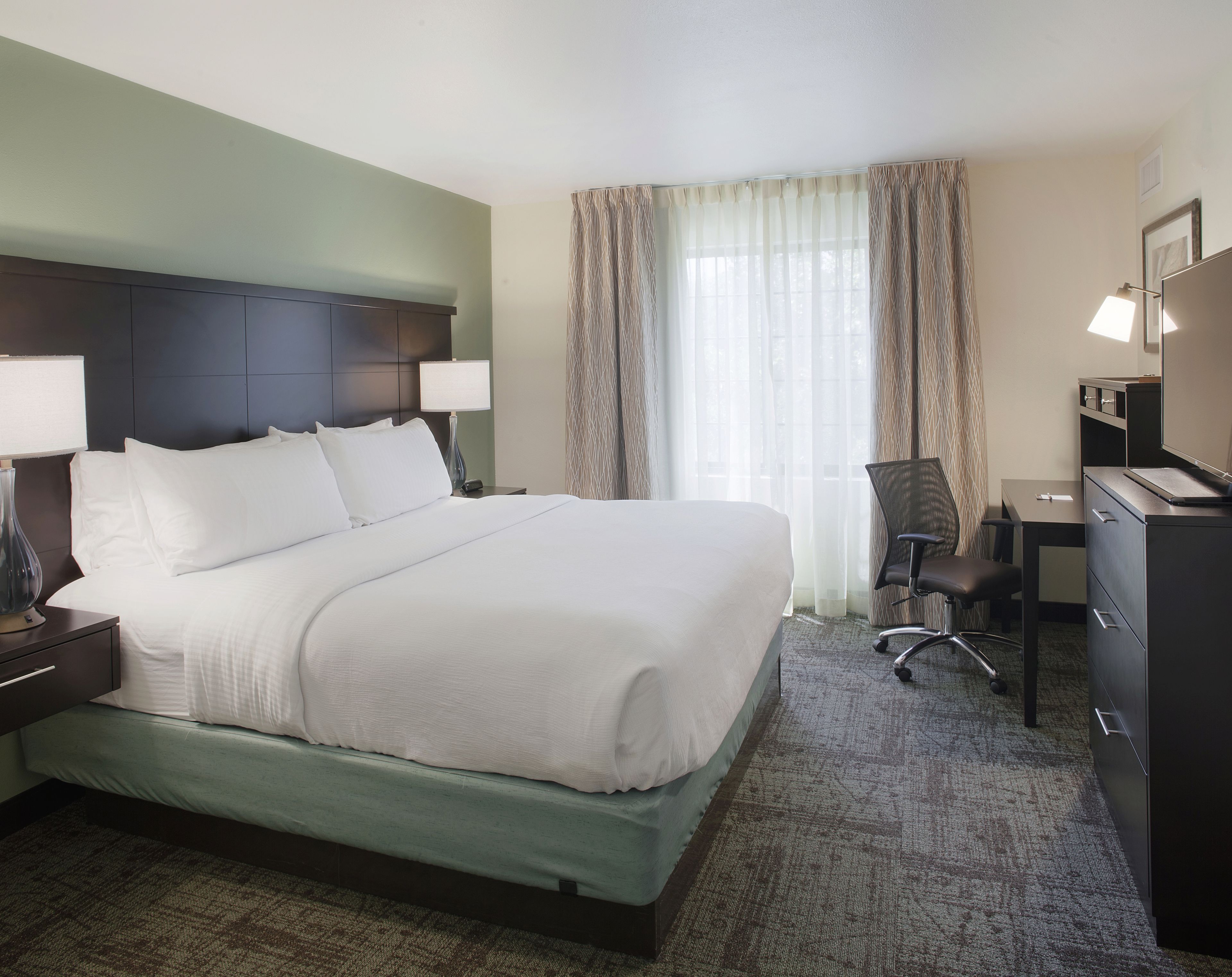 Une chambre d’hôtel avec un grand lit, un bureau, une chaise et une commode.