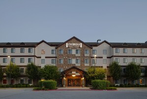 Un hotel Staybridge Suites con una fachada simétrica, varios ventanales y una entrada central con un arco acogedor.