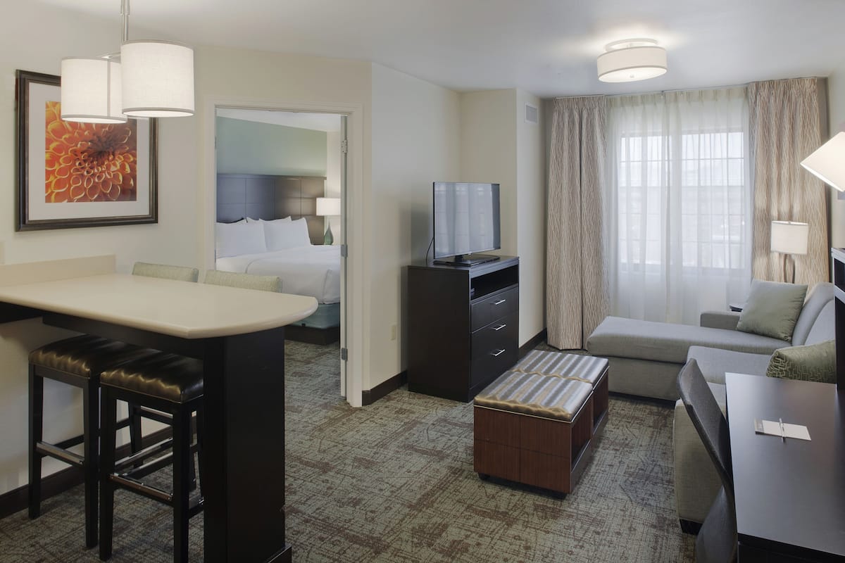 A hotel room with a kitchenette, a bed, a TV, a sofa, and a desk.