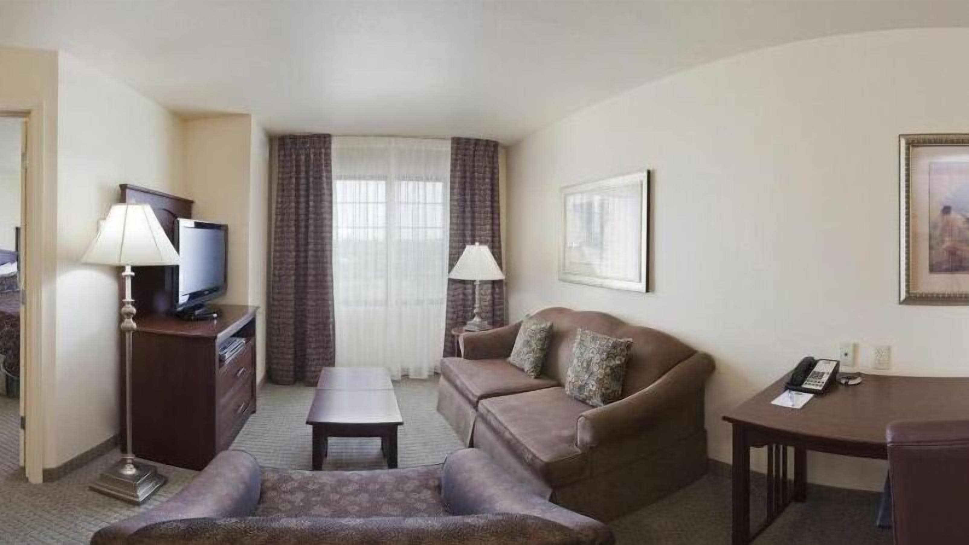 Hotelkamer met een bank, een klein tafeltje, een televisie, een lamp, een ingelijst schilderij en een telefoon op een bureau.