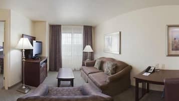 Habitación de hotel con sofá, una mesita, televisor, lámpara, un cuadro enmarcado y teléfono sobre un escritorio.