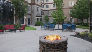 A courtyard with outdoor seating, a stone fire pit, and a multi-story building with windows and a stone facade. - Staybridge Suites Fayetteville/Univ Of Arkansas by IHG (Fayetteville)