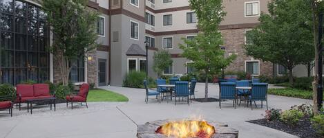 Un patio con mobiliario exterior, un hogar de piedra y un edificio de varios pisos con ventanas y fachada de piedra.
