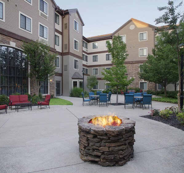 A courtyard with outdoor seating, a stone fire pit, and a multi-story building with windows and a stone facade. - Staybridge Suites Fayetteville/Univ Of Arkansas by IHG (Fayetteville)