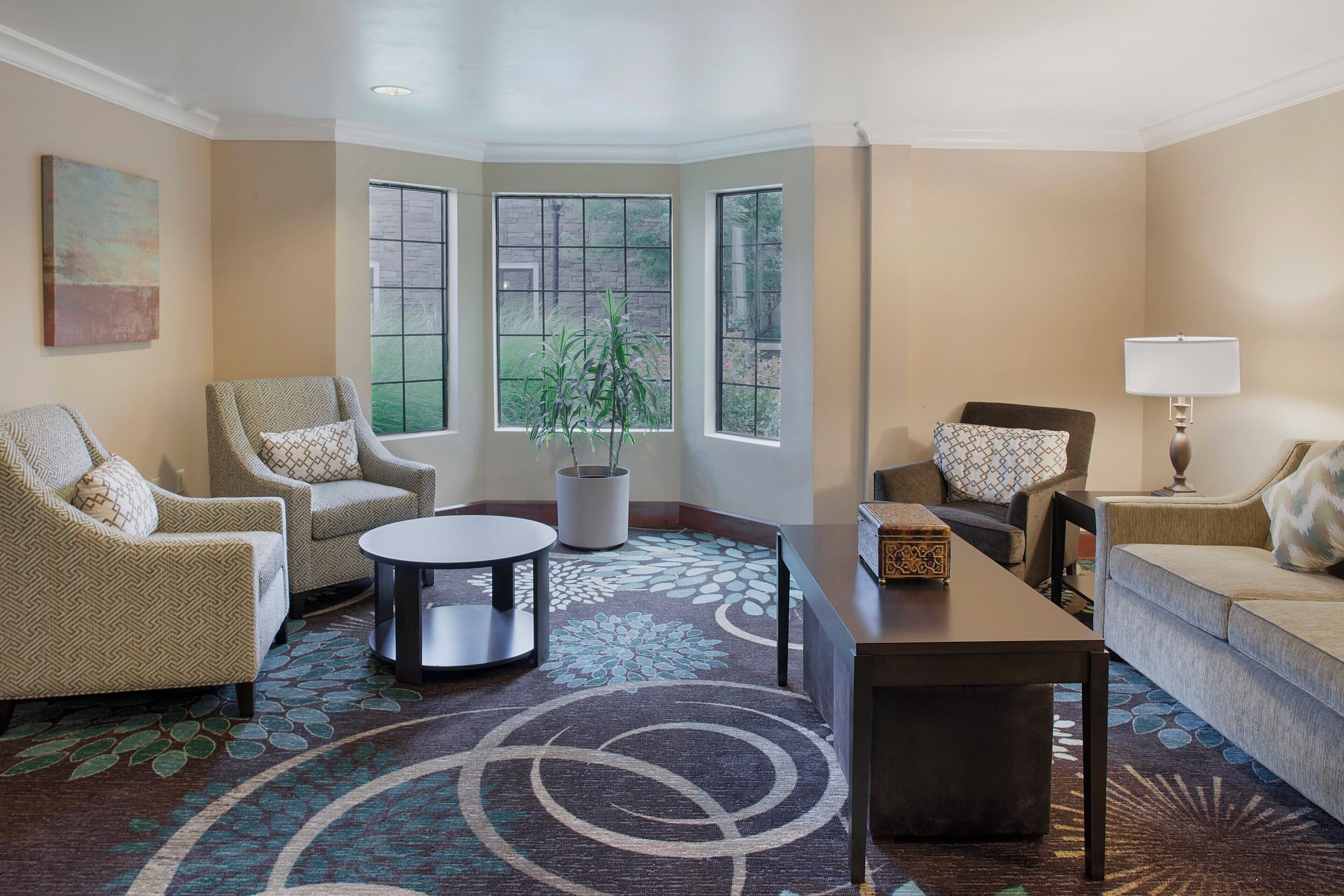 A living room with a round coffee table, two armchairs, a sofa, a lamp, and a potted plant.