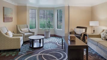 A living room with a round coffee table, two armchairs, a sofa, a lamp, and a potted plant.