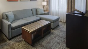 A modern living room with a grey sectional sofa, a wooden ottoman, a flat-screen TV, and three abstract wall art pieces. - Staybridge Suites Fayetteville/Univ Of Arkansas by IHG (Fayetteville)